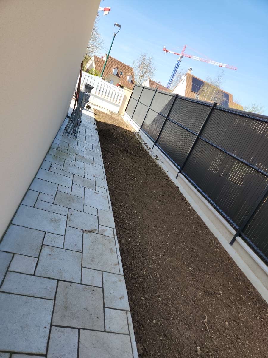 Allée pavée latérale entre maison et clôture à panneaux sombres