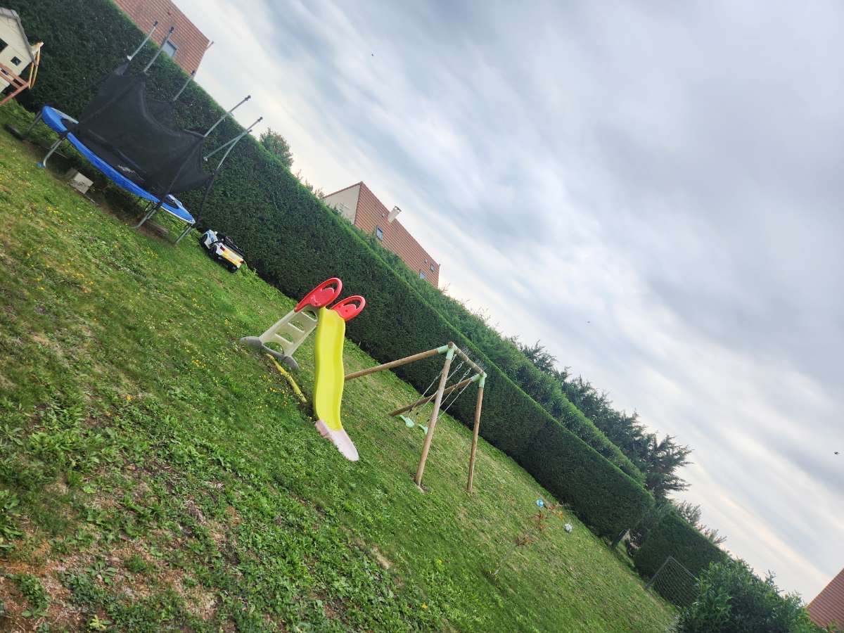Jardin familial avec haie taillée, aire de jeux et pelouse verte